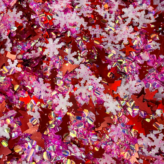 Close-up of Sleigh Belle craft glitter featuring metallic red Christmas trees, white snowflakes and pink iridescent pieces.