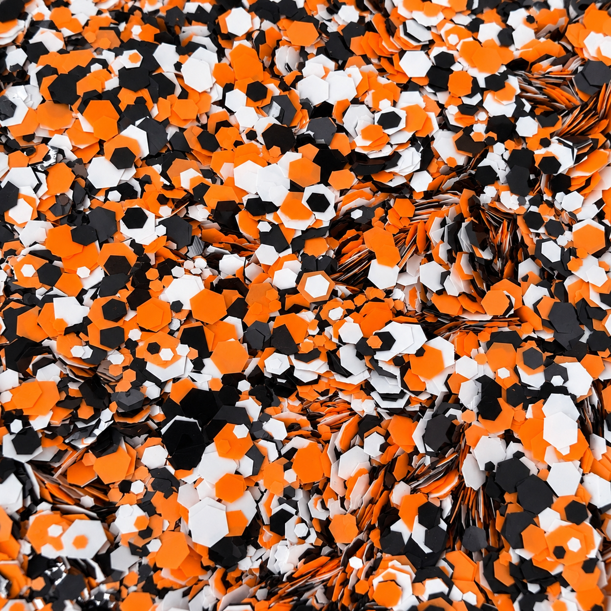 Close-up of Tangerine Twist craft glitter showing mixed-size orange, black and white hexagons.
