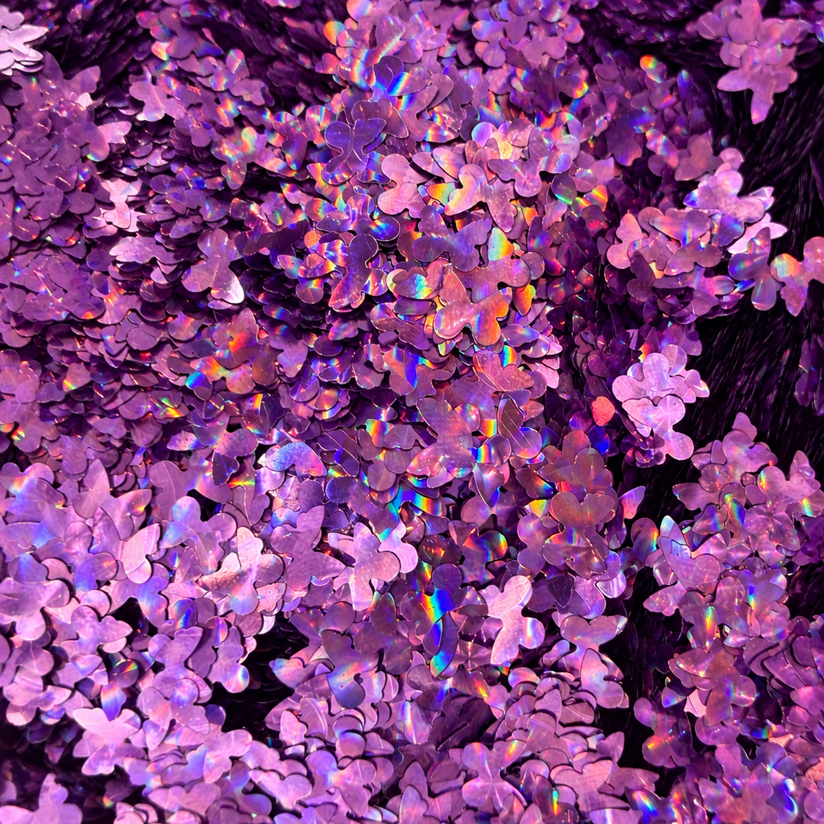 Close-up of Violet Wings craft glitter showing lilac and purple butterfly shapes with rainbow holographic reflections.