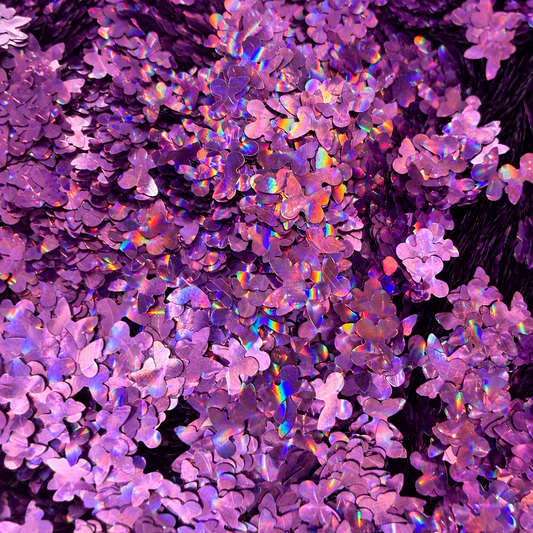 Close-up of Violet Wings craft glitter showing lilac and purple butterfly shapes with rainbow holographic reflections.