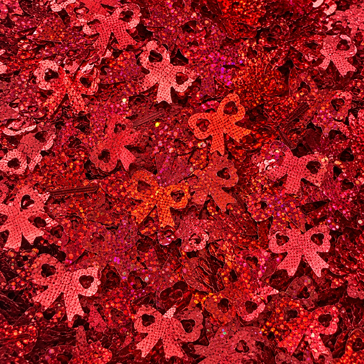 Close-up of Ribbon Romance craft glitter showing metallic red bows with heart-shaped cut-outs and holographic reflections.