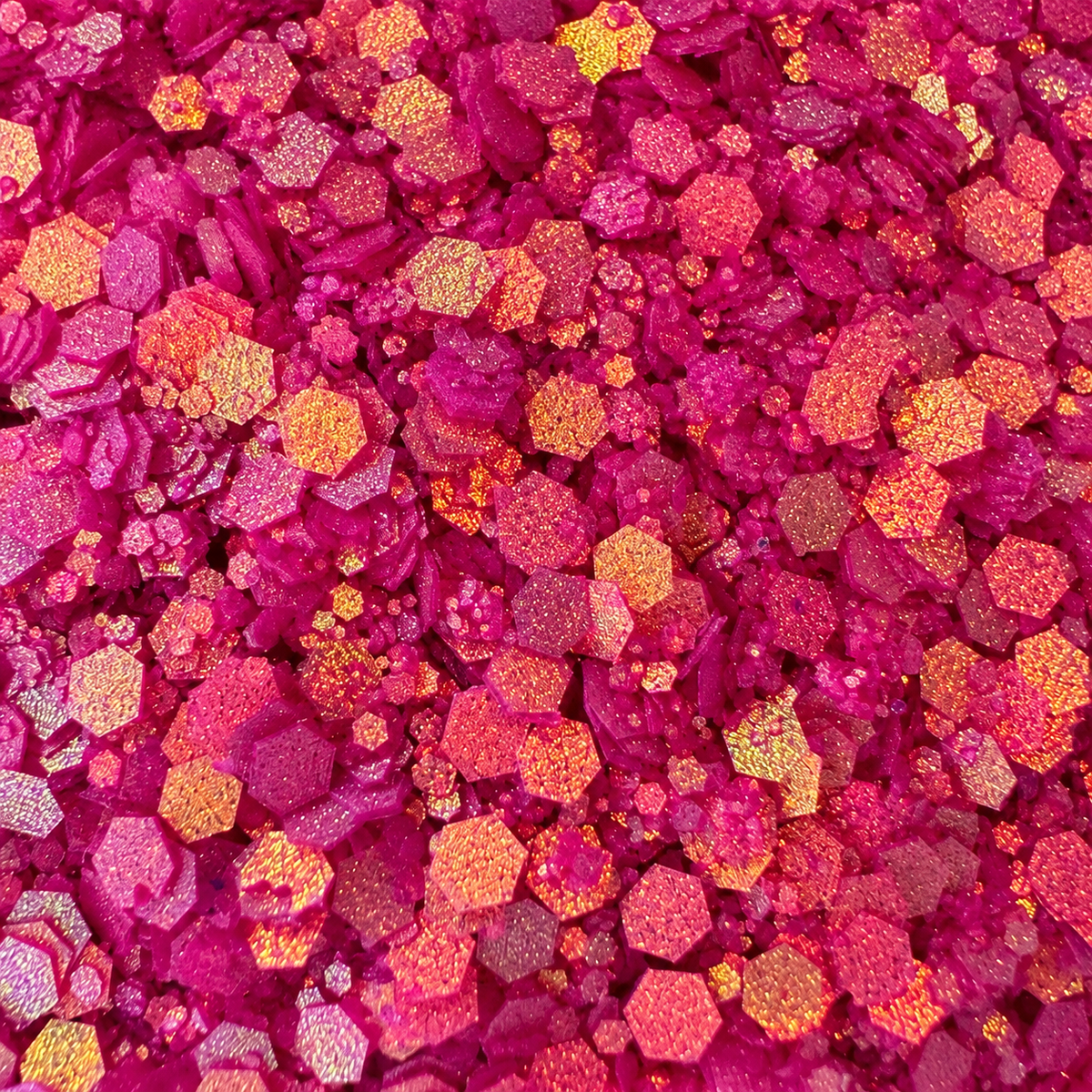 Close-up of Pink Inferno craft glitter showing mixed-size fuchsia-pink hexagons with warm golden and peach reflections.