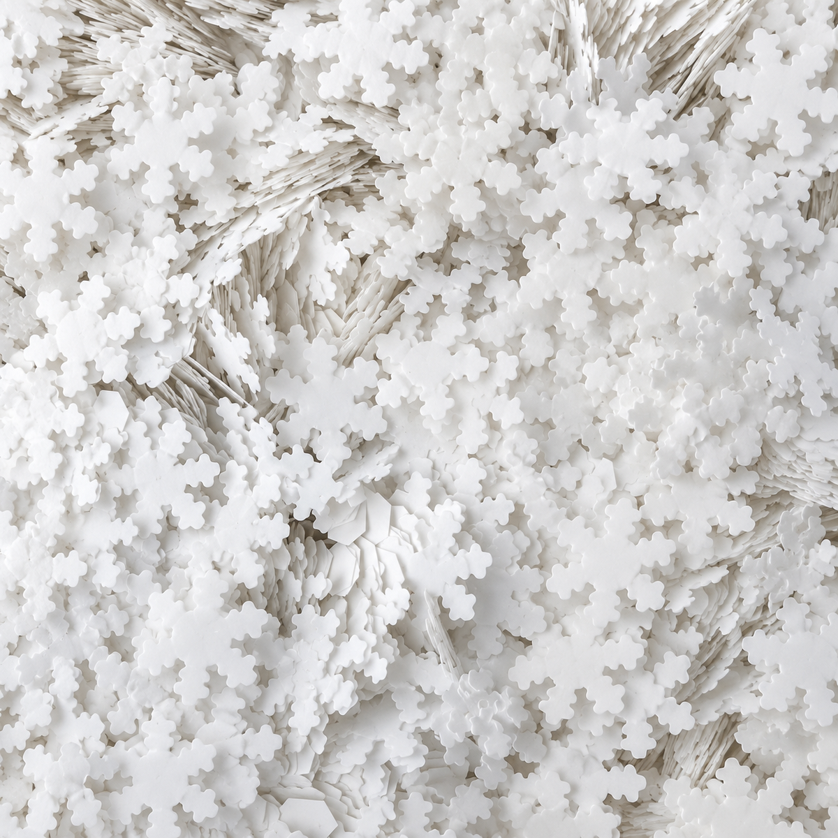 Close-up of Snowfall craft glitter showing overlapping opaque white snowflake shapes.